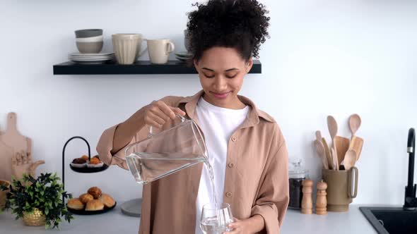 Happy Healthy African American Girl in Casual Clothes Standing at Home in the Kitchen Pouring Clean