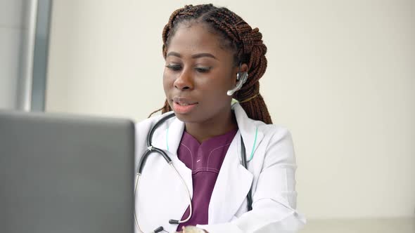 Young African American Woman Doctor with Headset Having Chat or Consultation on Laptop