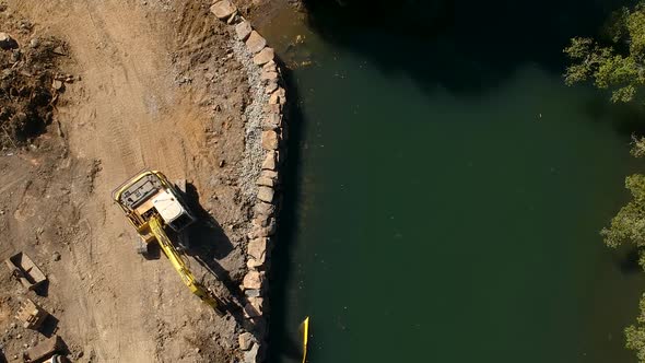 Arial view of a large excavator repairing a section of river damaged by a flood waters caused by a t