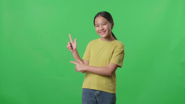 The Inspired Asian Kid Girl Smile And Pointing To The Side While Standing In The Green Screen Studio