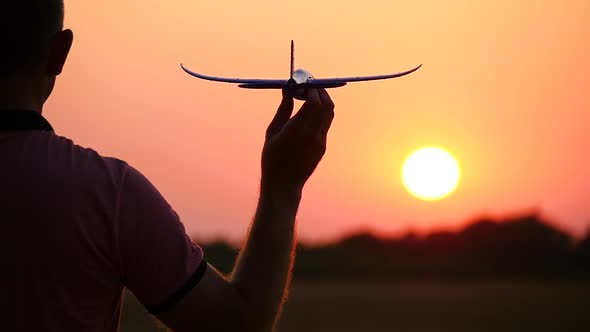 Silhouette of a Men Holding in Hand a Model Airplane, Standing in Front of the Sun at Sunset