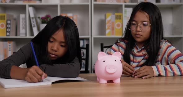 Two girls saving money with pink piggy bank