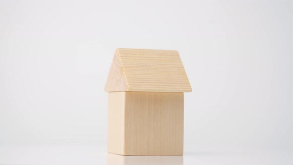 A toy house made of a wooden cube and a triangle in the form of a roof rotates on a white background