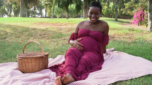 Young African woman caressing her pregnant belly while doing a picnic in park