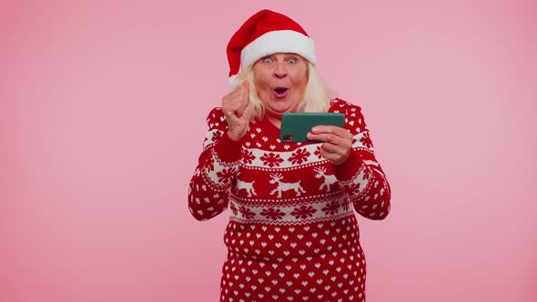 Worried Grandmother in Christmas Sweater Enthusiastically Playing Racing Video Games on Mobile Phone