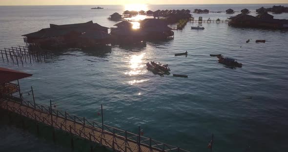 Aerial flight over turquoise ocean, boats, and huts at sunset in Mabul, Malaysia