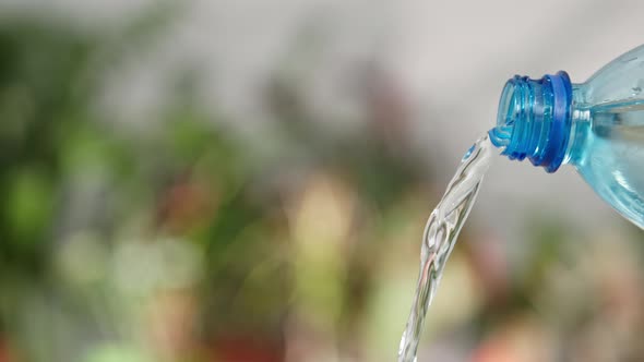 Clean Cool Water is Pouring a Plastic with a Transparent Blue Bottle on a Green Background Closeup