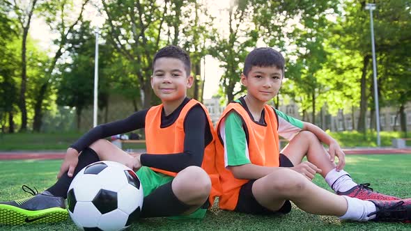 Football Players in Orange Vests Sitting on the Artificial Turf and Posing on Camera