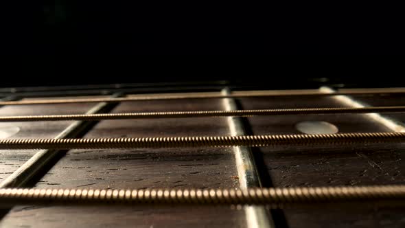 Slider Macro Shot of an Acoustic Guitar Neck with Metal Strings and Frets on a Black Background