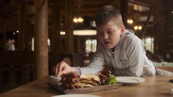 boy sits at table in restaurant and eats French fries. Boy soaks potatoes in red ketchup