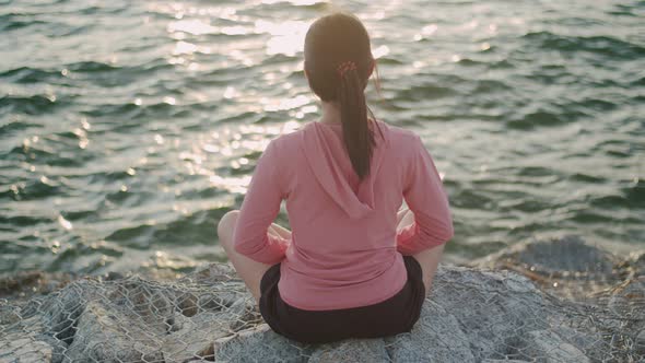Asian athletic female meditating sitting on stones seaside while beautiful sunset.