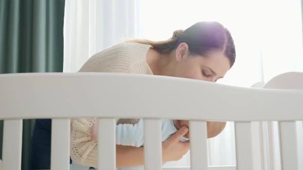 Caring Young Mother Holding Her Baby and Putting in Cradle