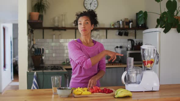 Portrait of mixed race female vlogger making fruit juice in the kitchen at home