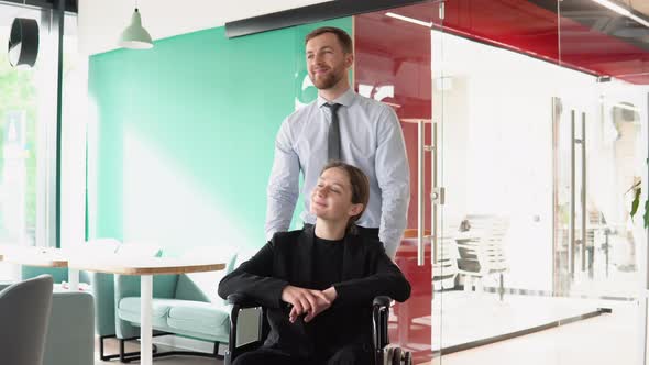 Young Man Pushing Wheelchair with Colleague in the Office