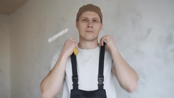 A Man in Construction Overalls Happily Shows a Paint Roller To the Camera