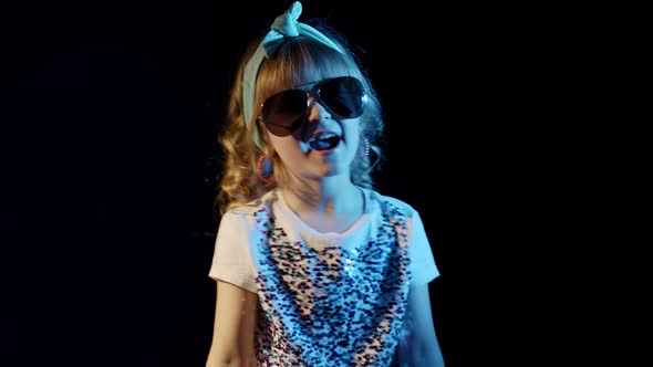 Playful Blond Girl in Blue Neon Lights Singing on Black Background Making Faces Fooling Around