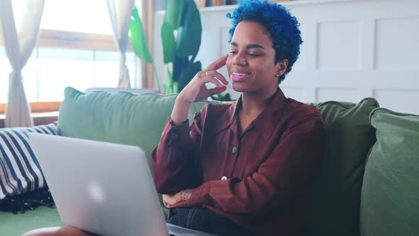 Young African American Woman Freelancer Sits on Sofa with Laptop on Lap