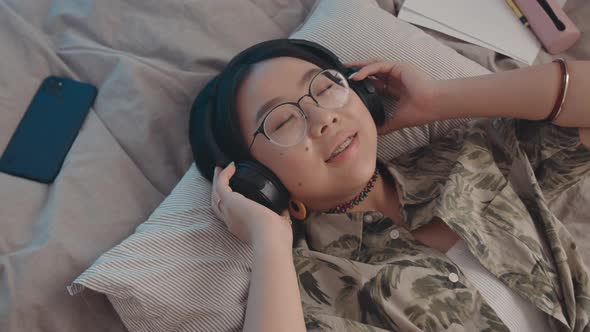Asian Teen Girl Listening to Music in Headphones in Bed