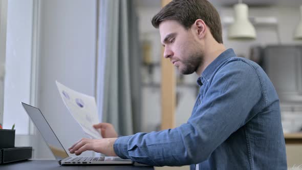 Beard Young Man Entering Data From Documents To Laptop