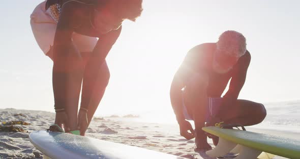 Happy african american couple preparing before surfing on sunny beach