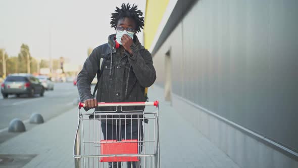 Portrait of Male Courier with Deadlocks in Covid Face Mask Pushing Shopping Cart To Shop