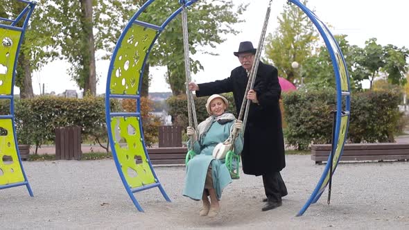 Senior couple on a playground, swinging on the swing set.