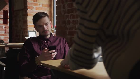 Young Handsome Man Drinking Tea and Using on the Cellphone in the Cafe