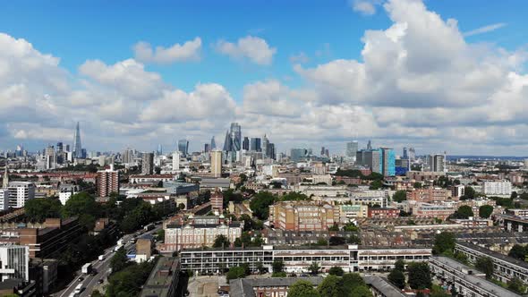 Reverse aerial shot of London skyline against white puffy clouds on a sunny summer day