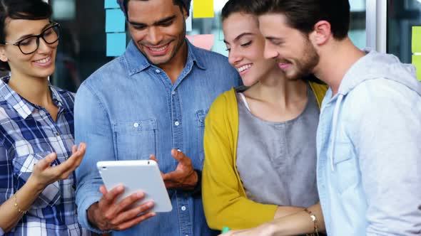 Smiling executives discussing over digital tablet during meeting