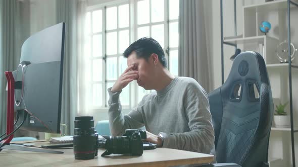 Asian Cameraman Tired While Using Desktop Computer For Working At Home