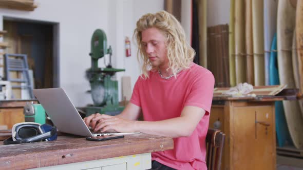 Caucasian male surfboard maker working on his laptop