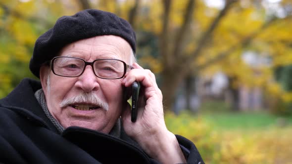 A Grandfather with a Gray Mustache and a Black Beret is Talking on a Smartphone