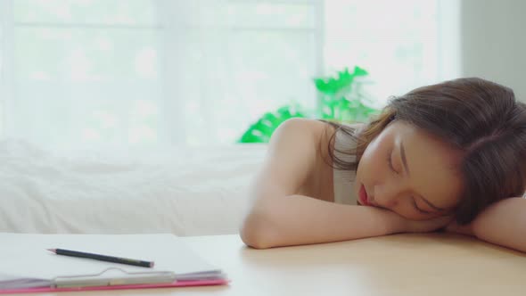 Over work Asian young woman sleep on work table in bedroom