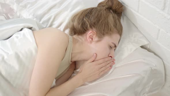 Top Down View Woman with Brown Curly Hair in Beige Tank Top Coughs in Bed in Morning