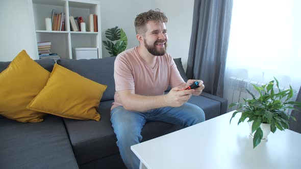 Attractive Man with Bristle and Toothy Grin Holding Joystick and Playing Videogames on Tv Sits at