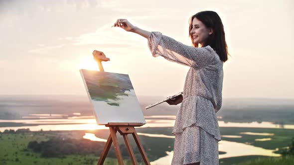 A Young Woman Artist Standing at Sunset and Drawing a Painting of Nature Landscape Measuring