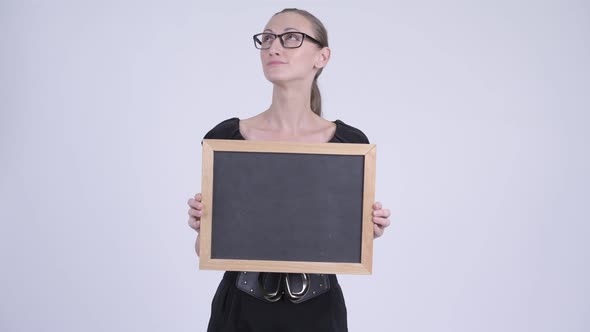Portrait of Happy Blonde Businesswoman Thinking While Holding Blackboard