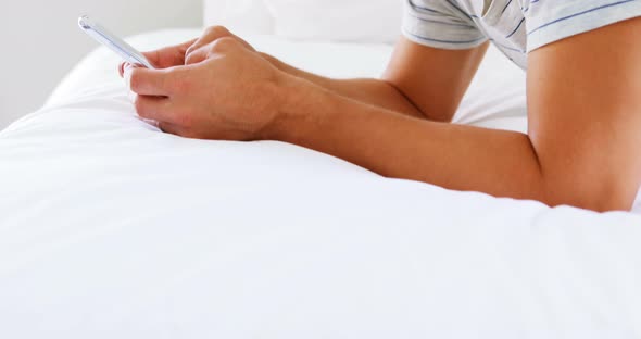 Smiling man using mobile phone on bed in bedroom