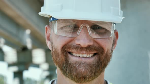 Close Up Portrait of Smiling Young Master Builder in Protective White Hard Hat Looking at Camera