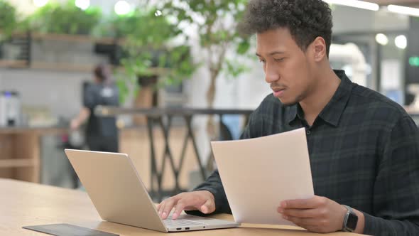 African American Man with Laptop Reading Documents