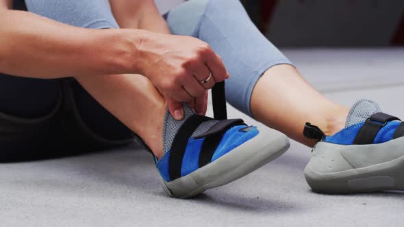 Low section of caucasian woman putting on climbing shoes at indoor climbing wall