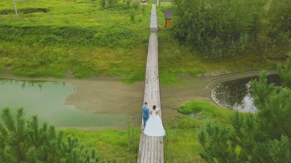 Just Married Couple Walks Along Bridge Over Stream Upper