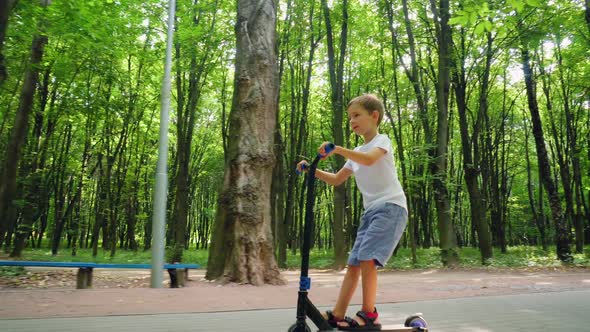 A Boy Rides a Scooter in a City Park