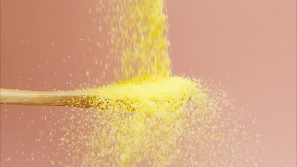 Falling Polenta on Wood Spoon on Pink Background Closeup