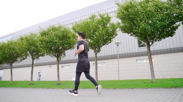 young asian man runner down the street on urban background of city park.