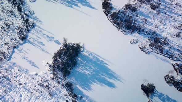 Aerial revealing birdseye view of snowy bog landscape with frozen lakes in sunny winter day, Dunika
