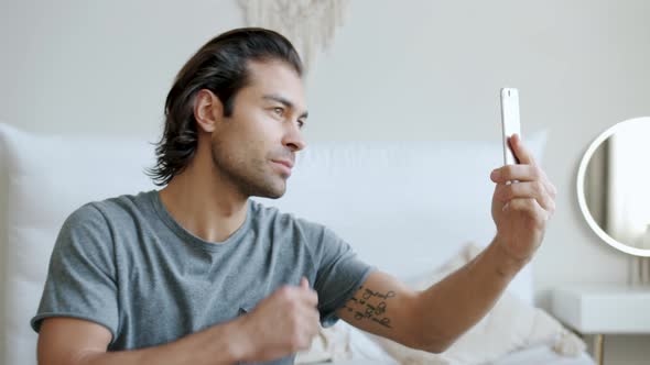 Slow Motion of Attractive Guy Posing for Smartphone Camera Taking Selfie in Bedroom
