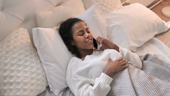 Top View of Young African Girl Talking on Phone in Bed