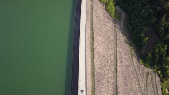 Aerial Top down Show of road splitting water and landscape with car driving in the middle