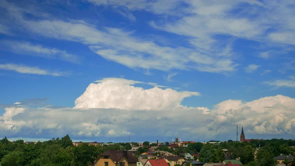 Time lapse of beautiful white fast moving puffy cumulus clouds on a sunny summer day, cityscape with alt